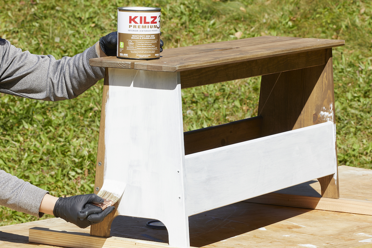 Woman paints stained wood bench with Kilz primer.