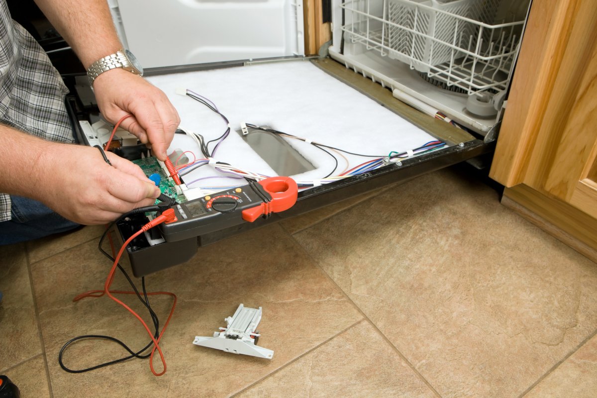 Using a multimeter tool to check the heater of empty dishwasher.