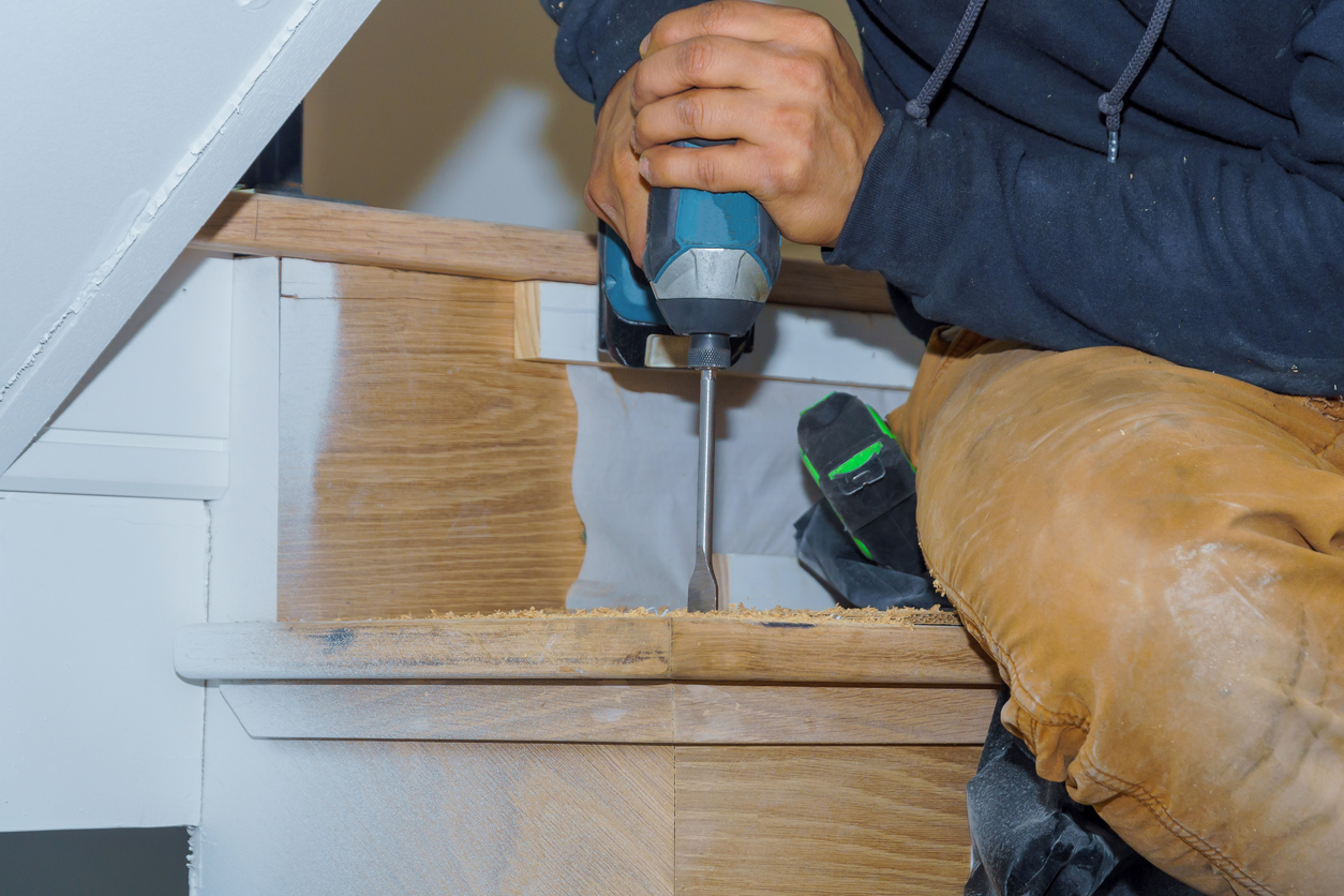 Man screws tread into riser with drill in wooden stairs