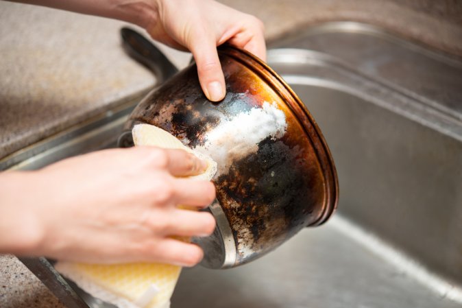 Wiping away rust from a metal saucepan over a kitchen sink