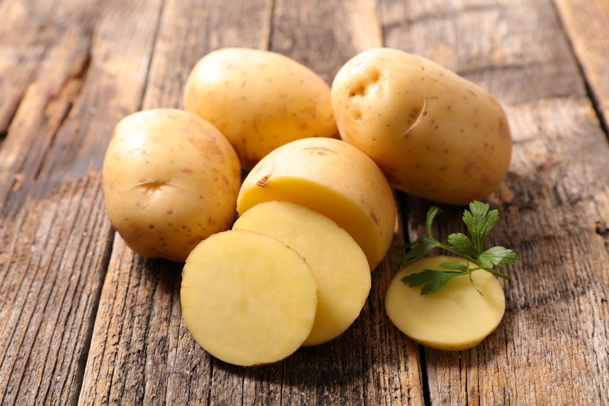 Partially sliced potato surrounded by whole potatoes and a parsley sprig