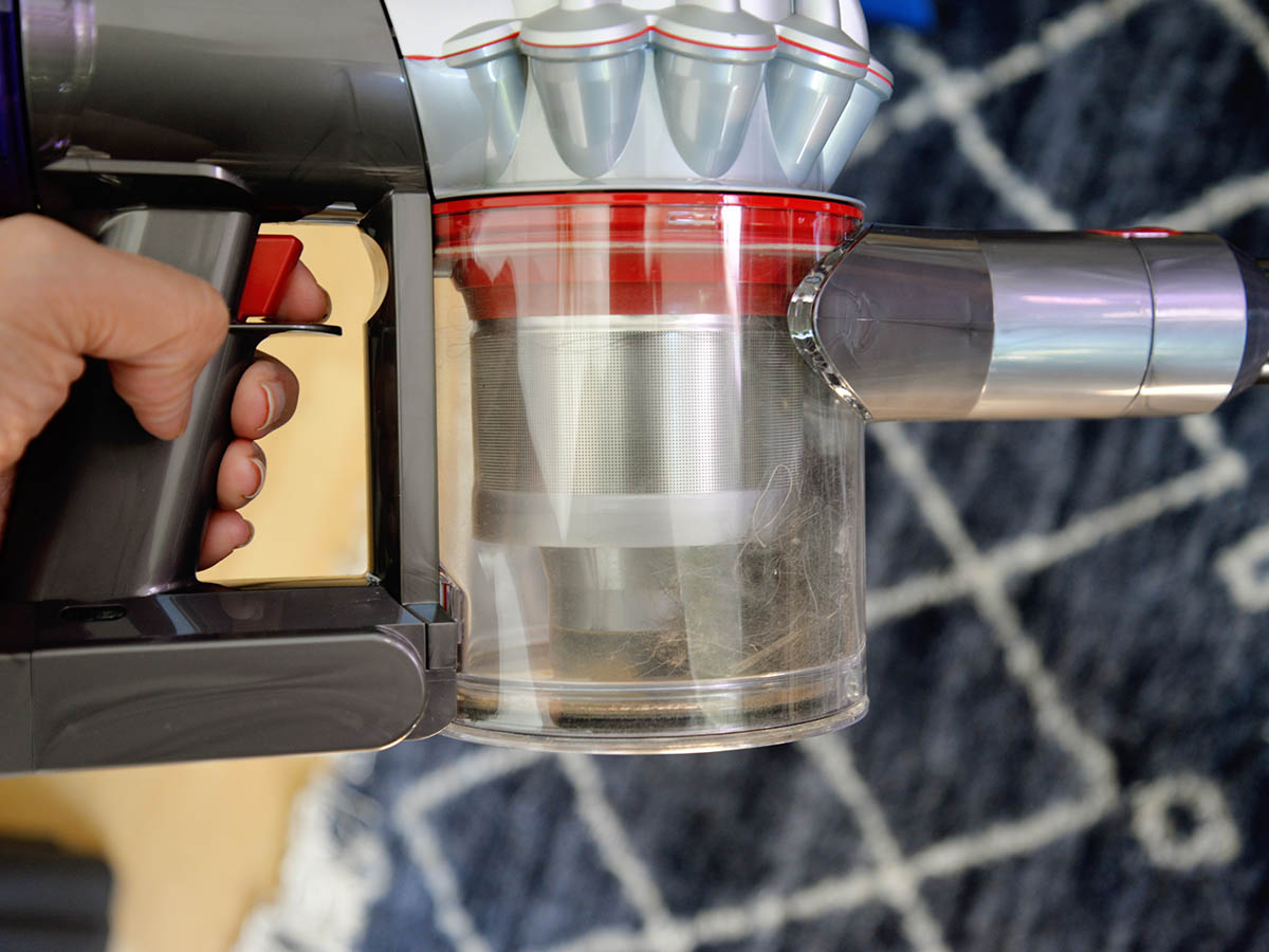 The empty dustbin, handle, and power trigger of a Dyson stick vacuum.