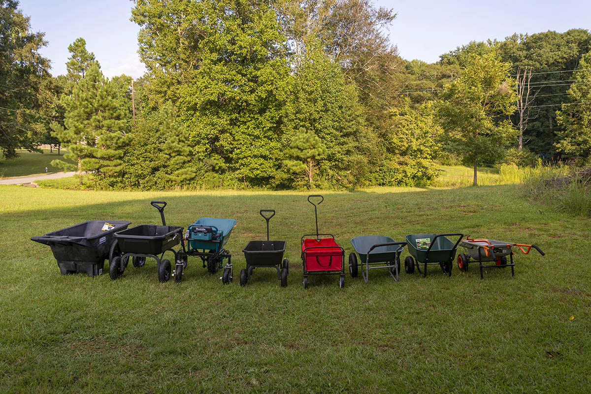 8 of the Best Wheelbarrow Options lined up on a huge grass lawn in the summer