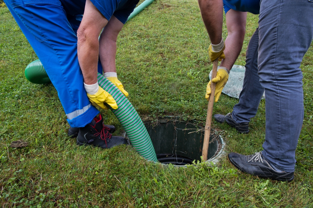 Two people holding a large green hose are pumping septic system.