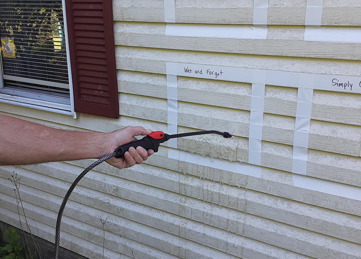 Person using power washer to spray vinyl siding cleaner off house