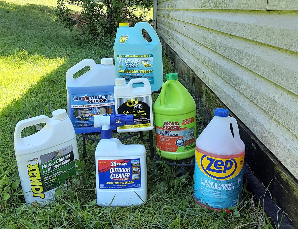 Seven bottles of the Best Vinyl Siding Cleaners on grass next to cream vinyl sided house