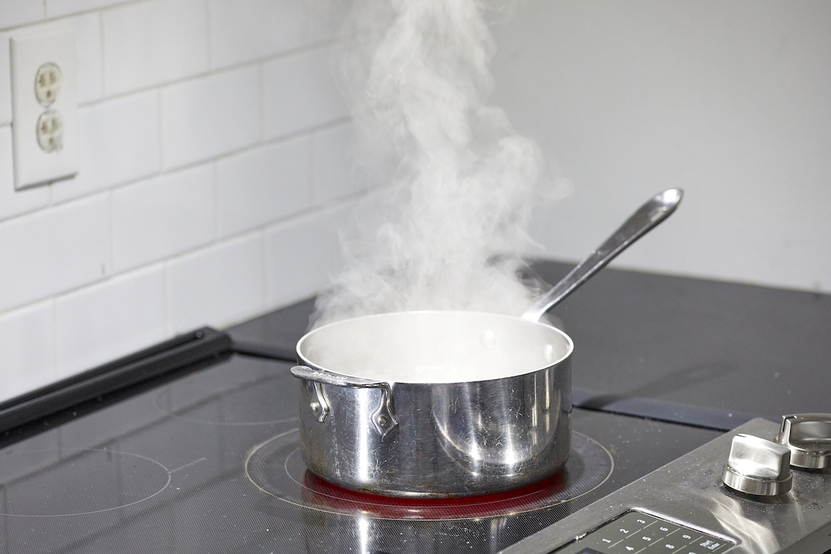 A small saucepan of water boils on a cooktop.