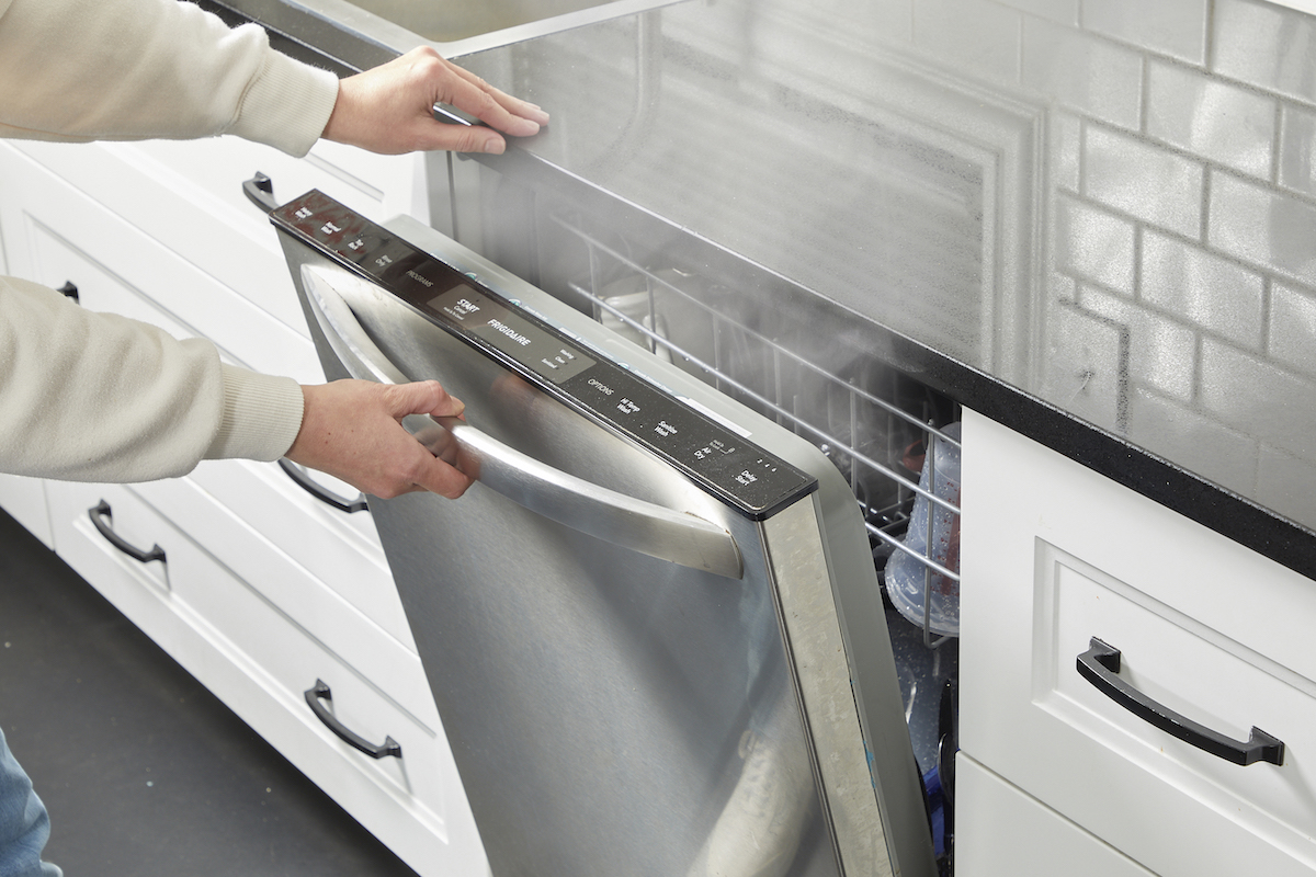 Woman opens a dishwasher and lots of steam comes out.