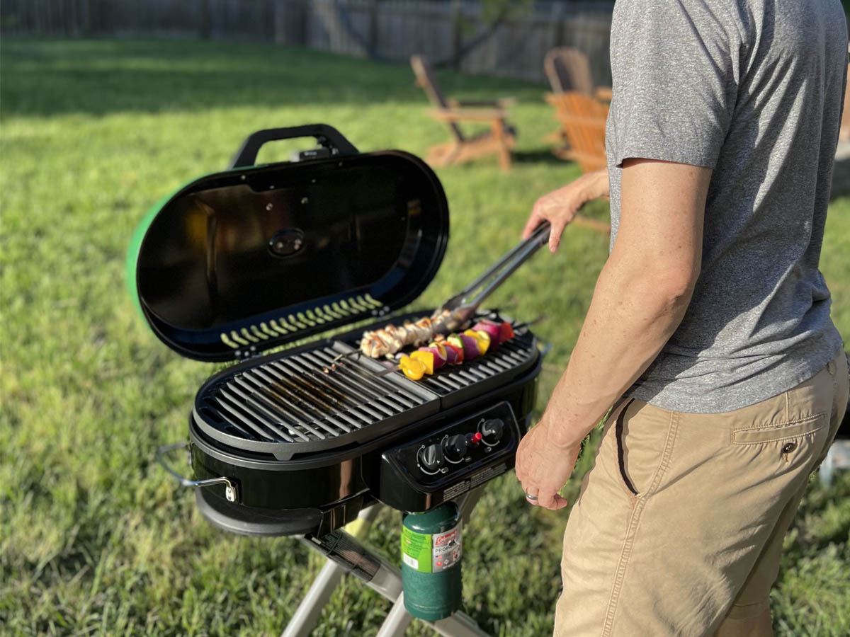 A person using the Coleman RoadTrip 285 Portable Stand-Up Propane Grill outdoors during testing.