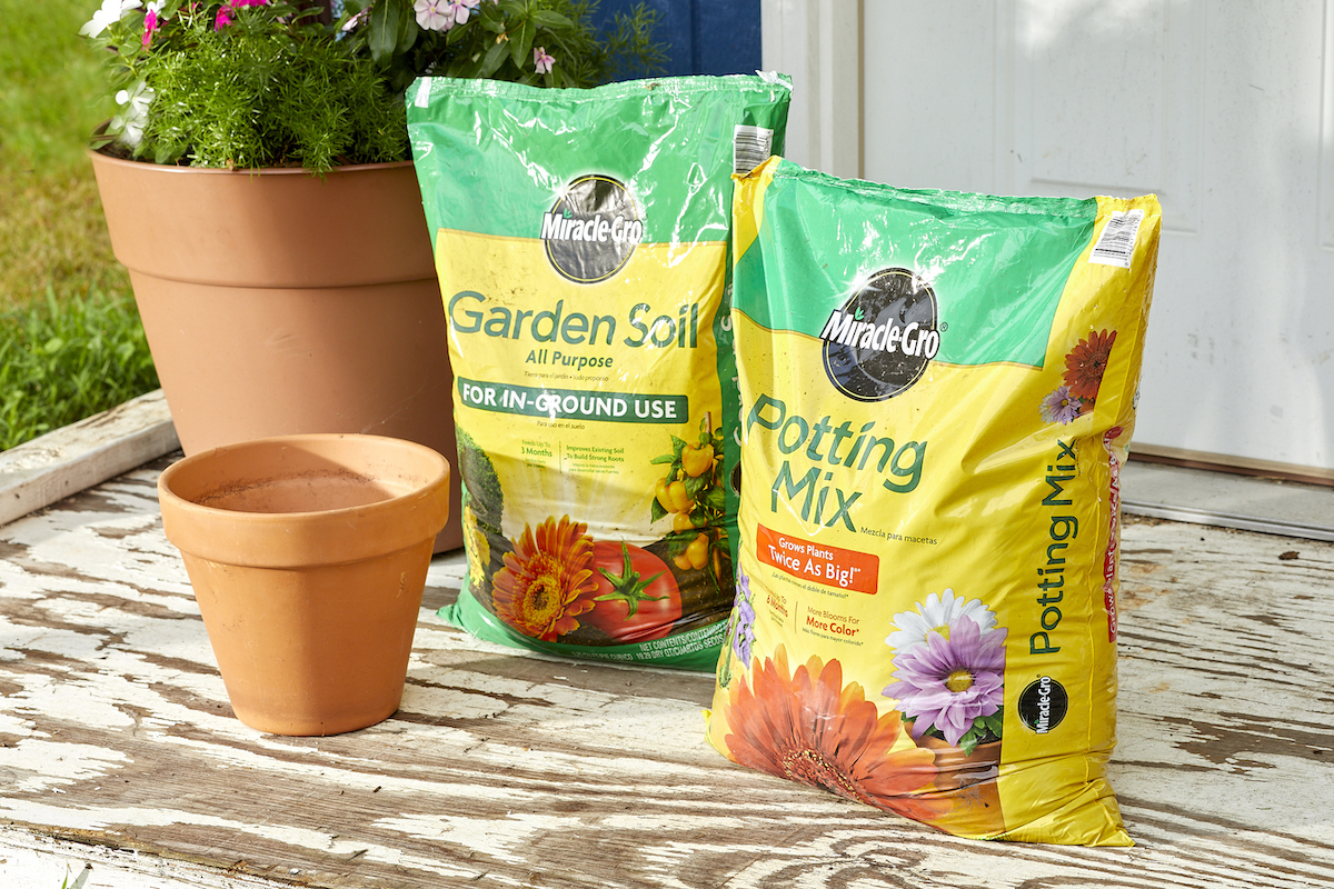 Bags of both potting soil and garden soil, side by side surrounded by a few terra cotta garden pots.