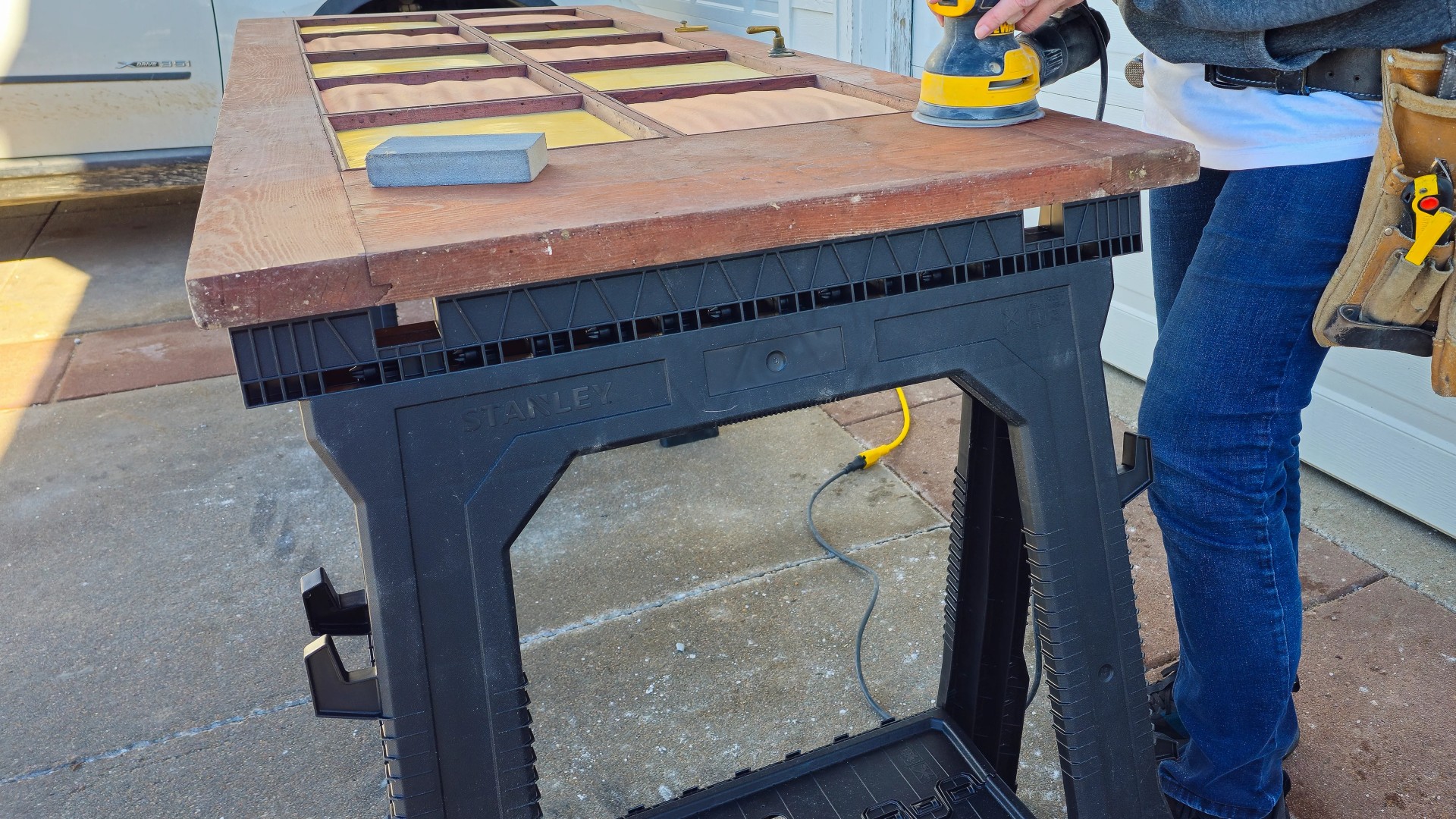 woman-sanding-door-random-orbit-sander-stanley-sawhorses.webp