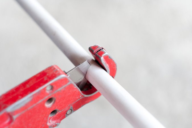 Cutting a PVC pipe with a pipe cutter.