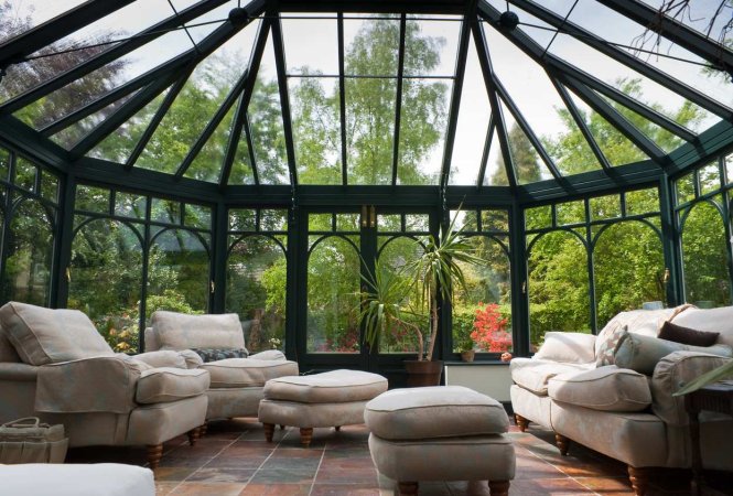 A sunroom made of glass with a tile floor and a full living-room furniture set.