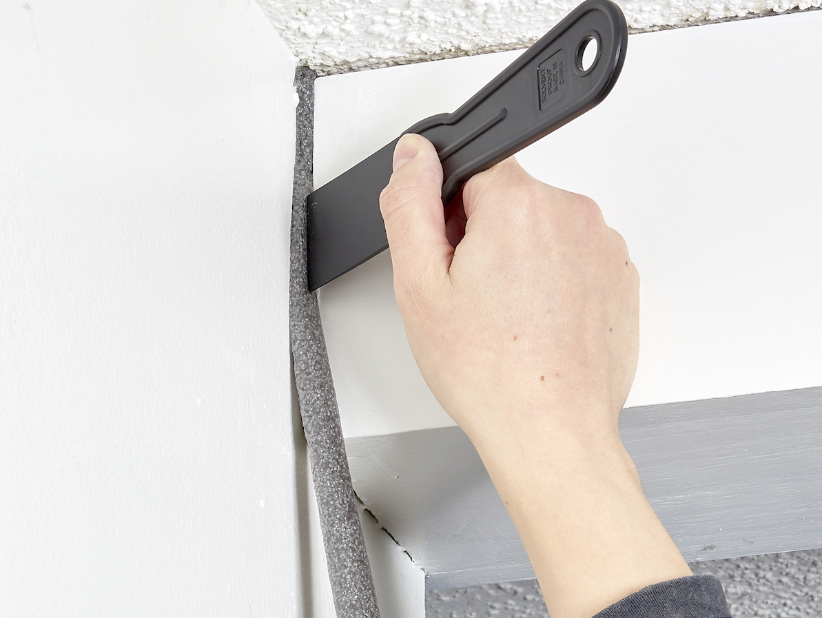 Woman uses a plastic putty knife to push backer rod into a large gap between bathroom walls. 