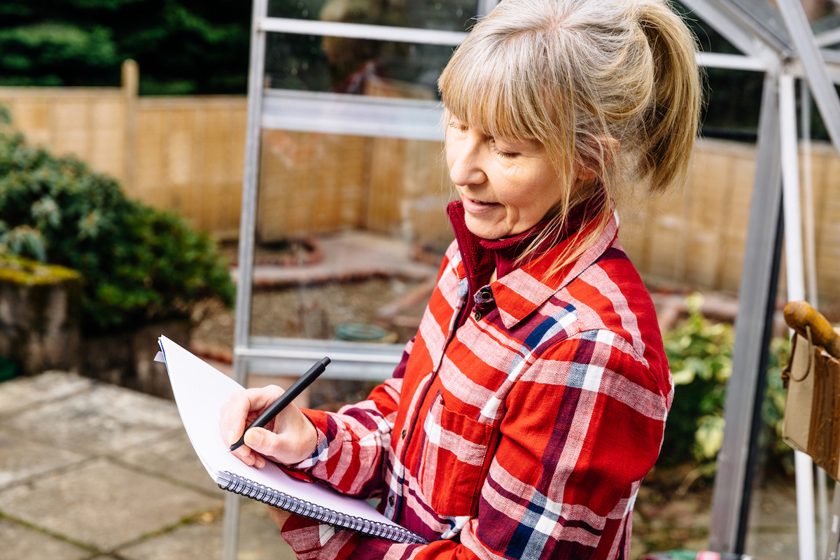 A woman is planning with a note pad and pen in her garden.