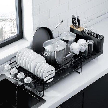  The Kitsure Dish-Drying Rack With Extendable Tray sitting on a kitchen counter next to a kitchen sink and loaded with drying dishes.