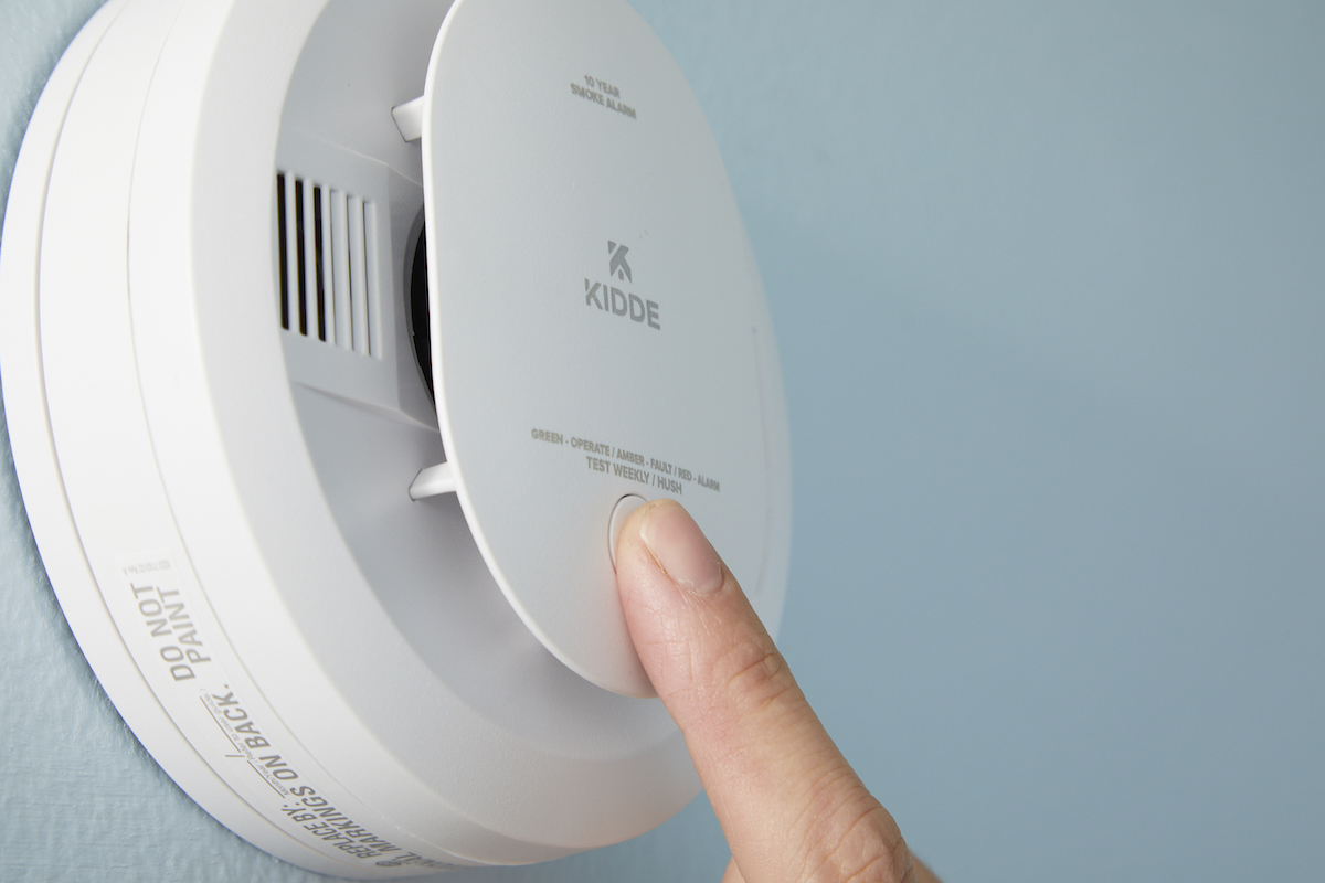 Woman pushes the "test" button on a smoke detector mounted to the wall.