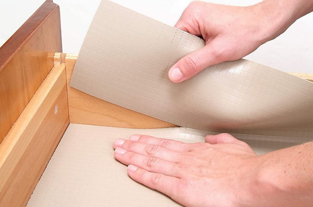 A person tearing the edge off a shelf liner to fit a drawer.