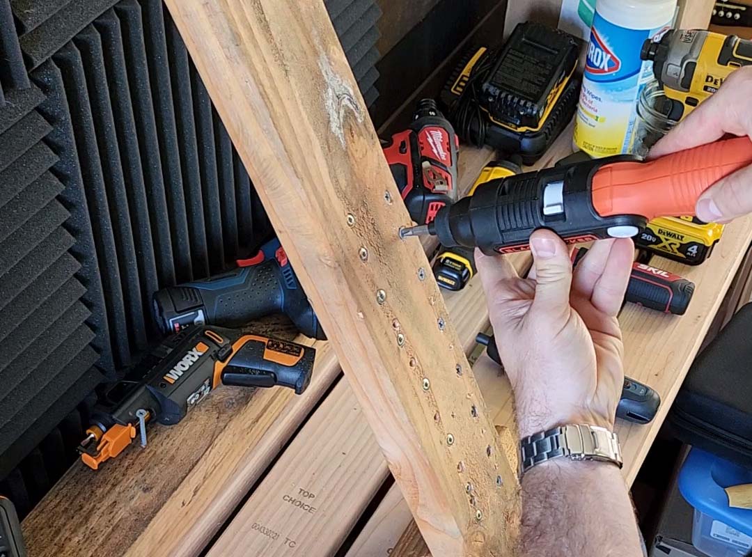 A person testing the best screwdriver option on a piece of wood with several other electric screwdrivers on a table in the background.