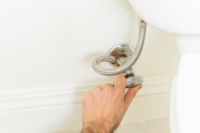 Person's hand turns the handle on the toilet shut-off valve.