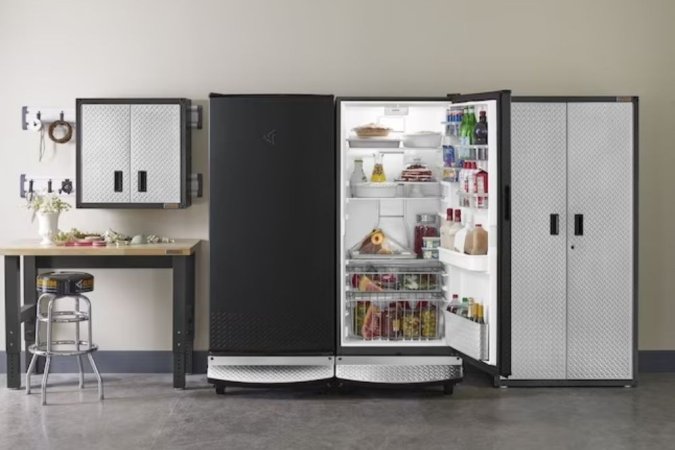 An upright freezer full of food between a workbench and storage cabinet.