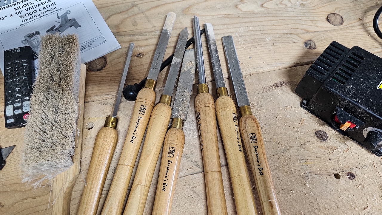 Image of wood lathe tools, brush, and power supply on wood work bench