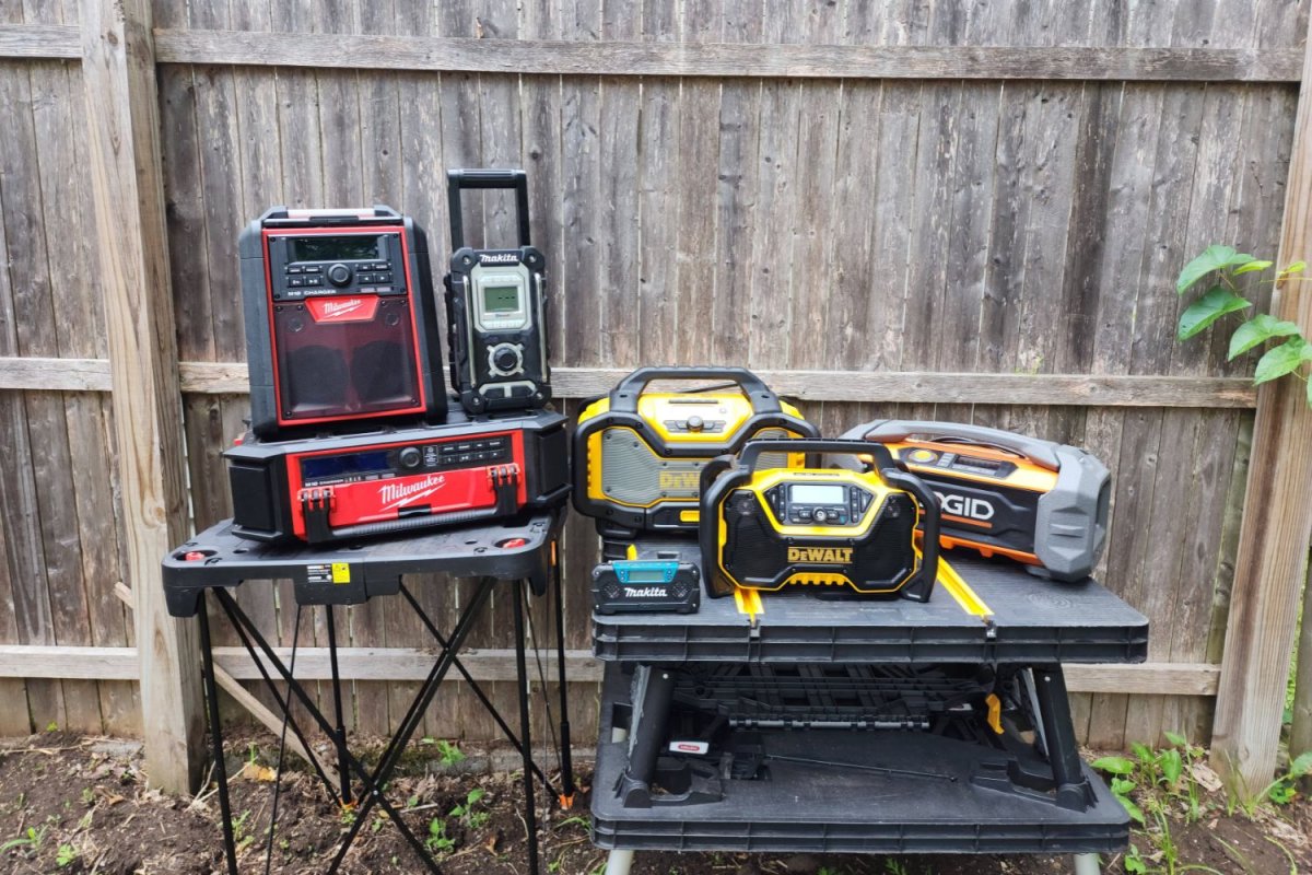 Seven jobsite radios on workbenches outside