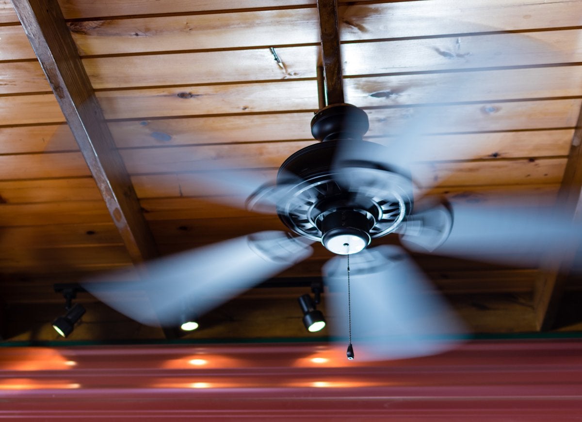 A a black spinning ceiling fan mounted on a wooden ceiling.