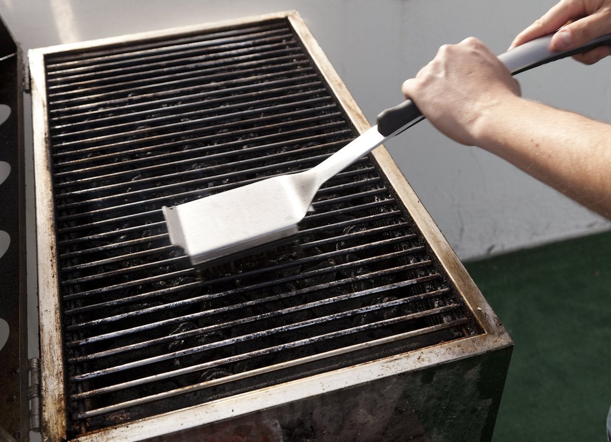 Scraping a grill with brush to clean off burnt grime.