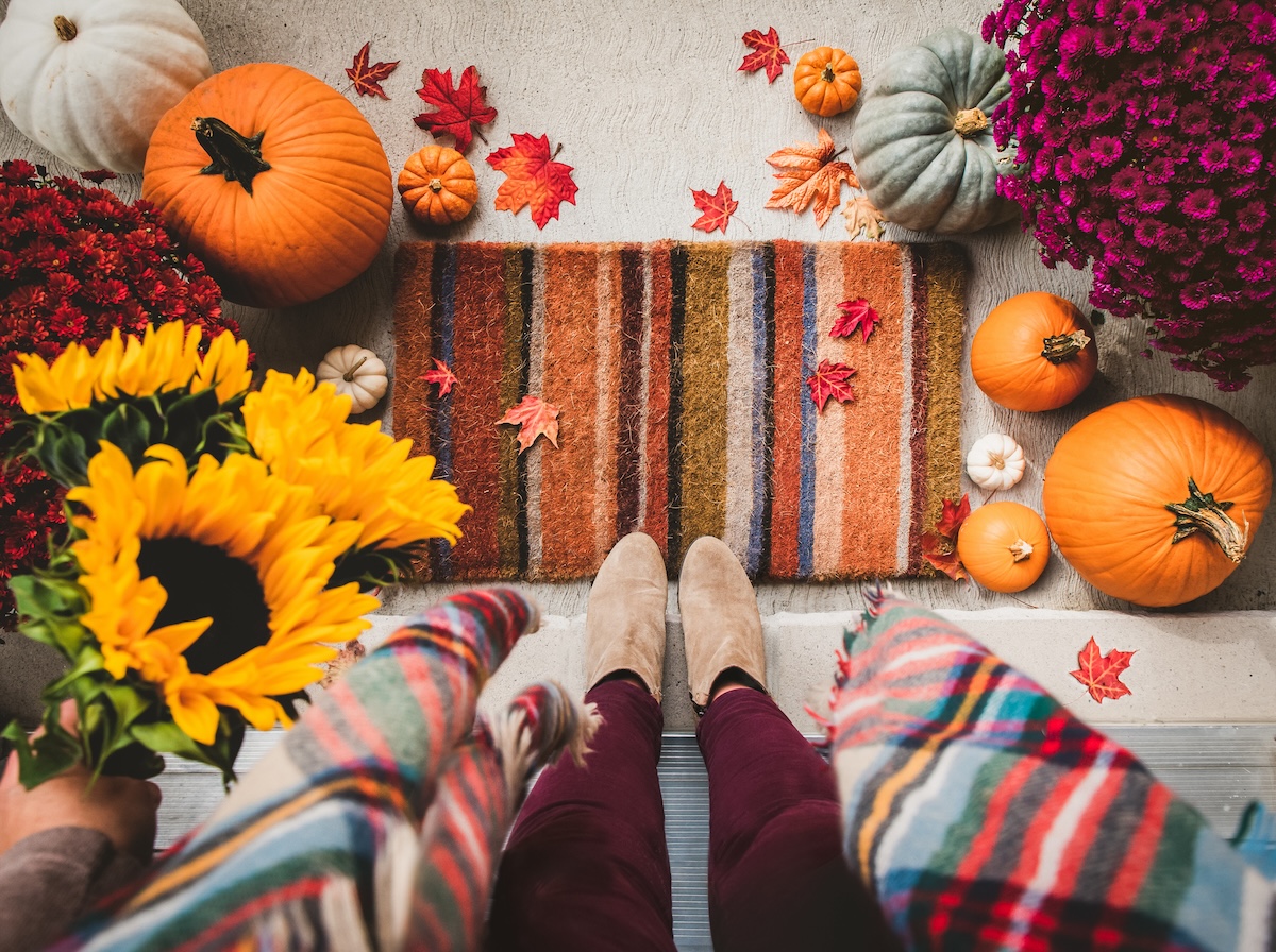 An autumn-themed doorstep with pumpkins, sunflowers, and a striped mat.