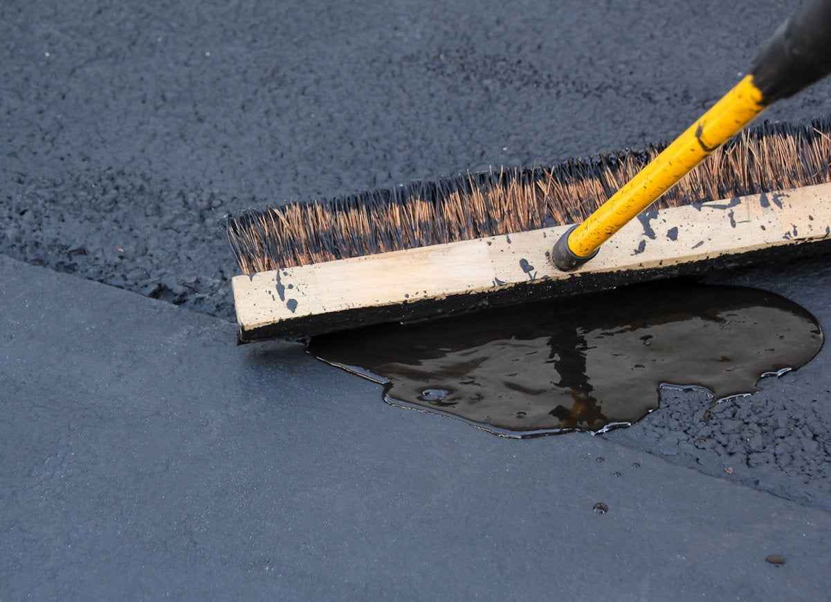 A broom moving around wet asphalt on a driveway.