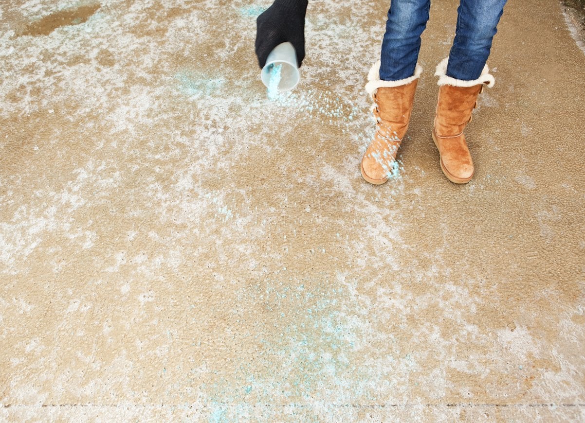 Person with brown suede boots spreads teal ice melt on a driveway.