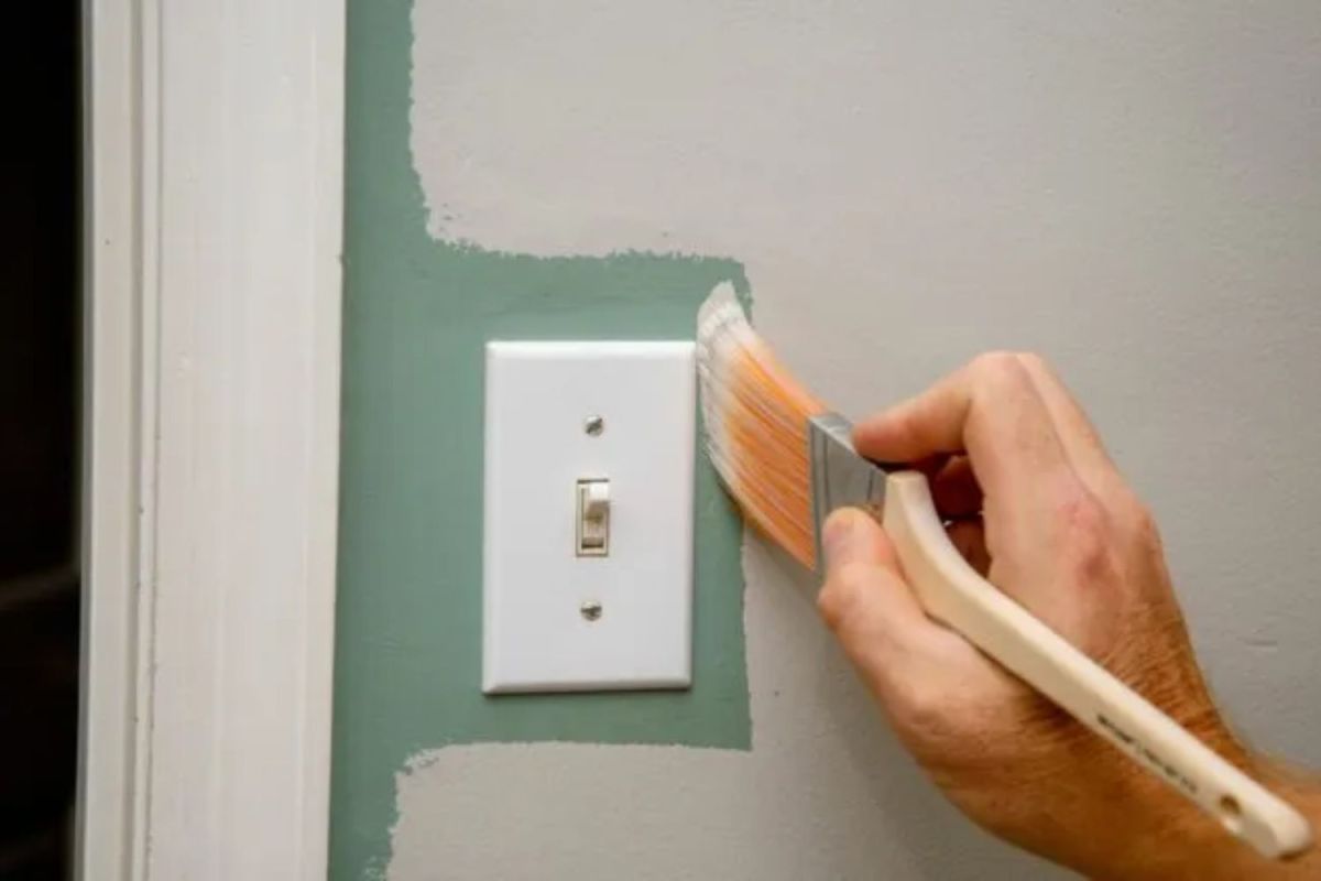 Someone painting around a light switch on a wall