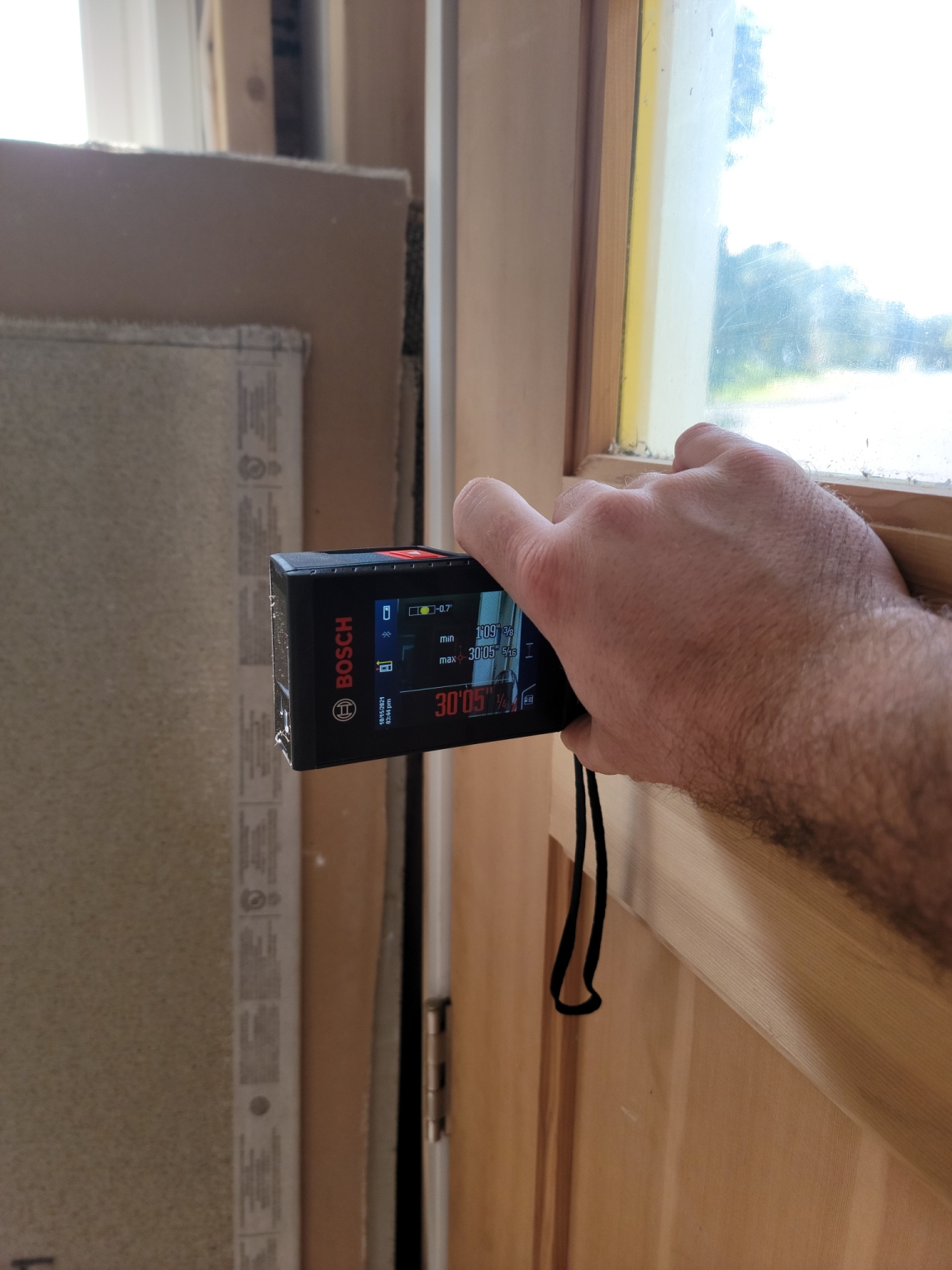 A person holding the best laser measure against a door and being pointed toward the center of a room.