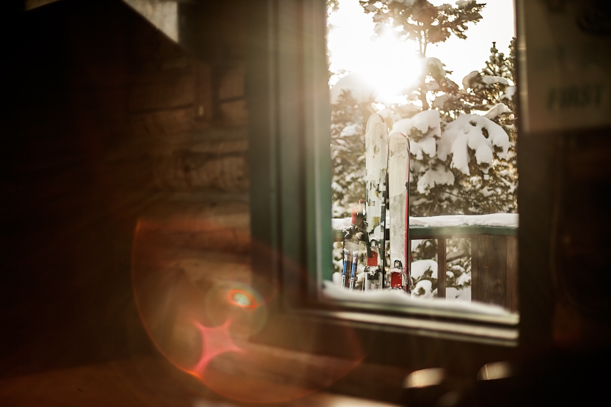 Sun streaming through a winter window with snow and skis outside.