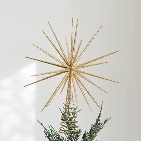  The Crate & Barrel Glitter Star Christmas Tree Topper on a tree with a white wall in the background.