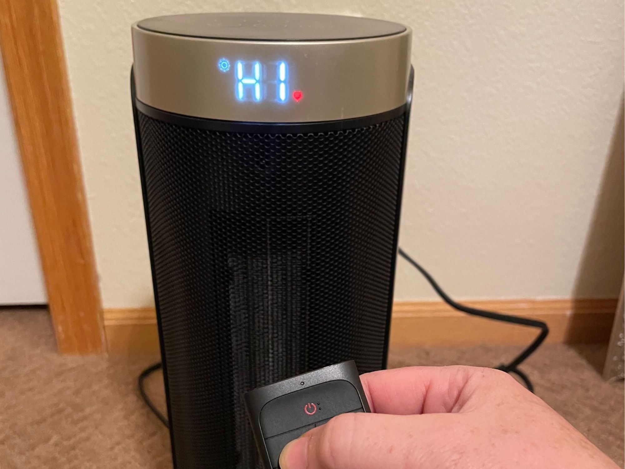 a hand with a remote control of one of the best electric heater options