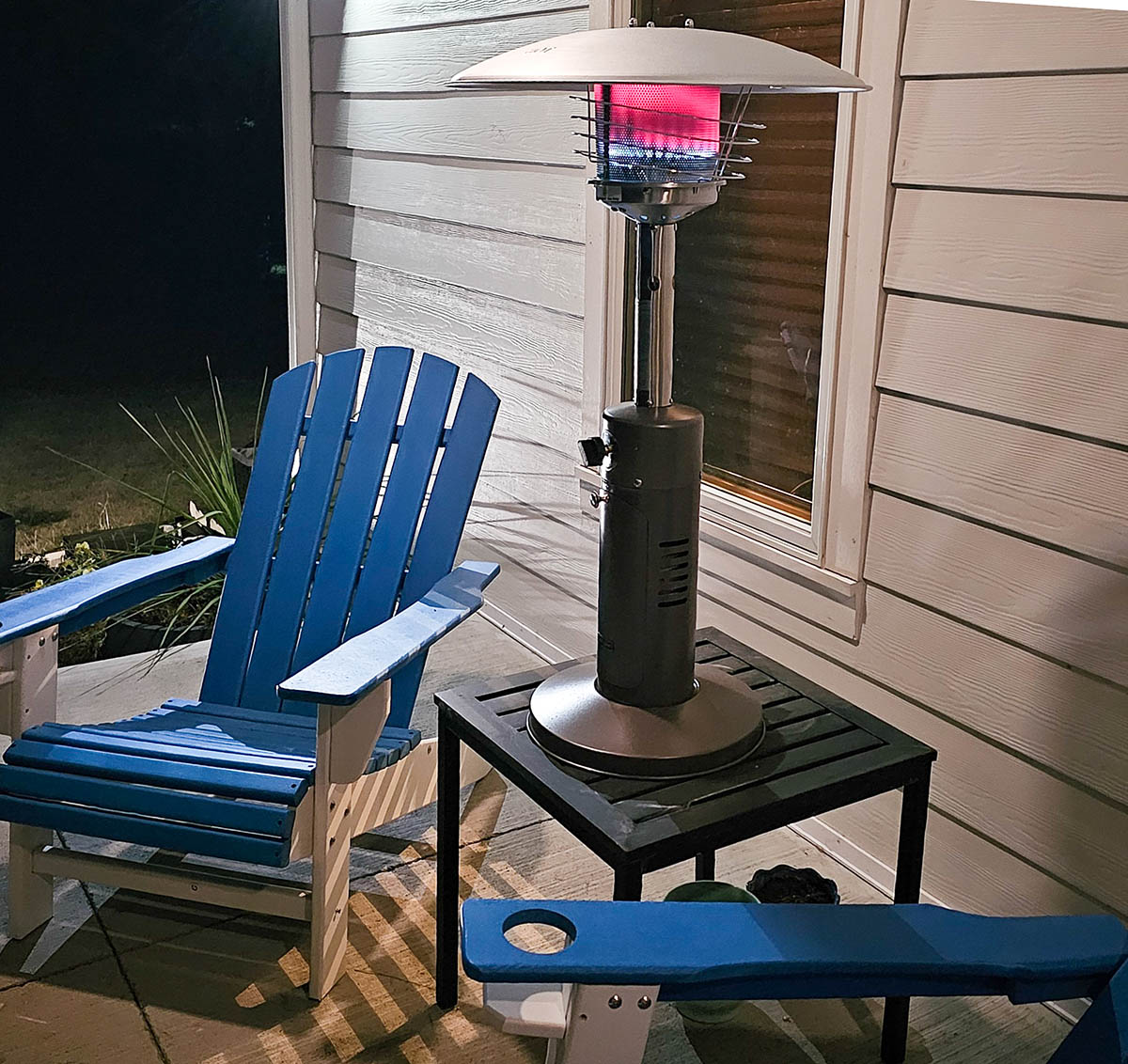 The Best Propane Heater set up on an outdoor side table between two chairs on a porch.