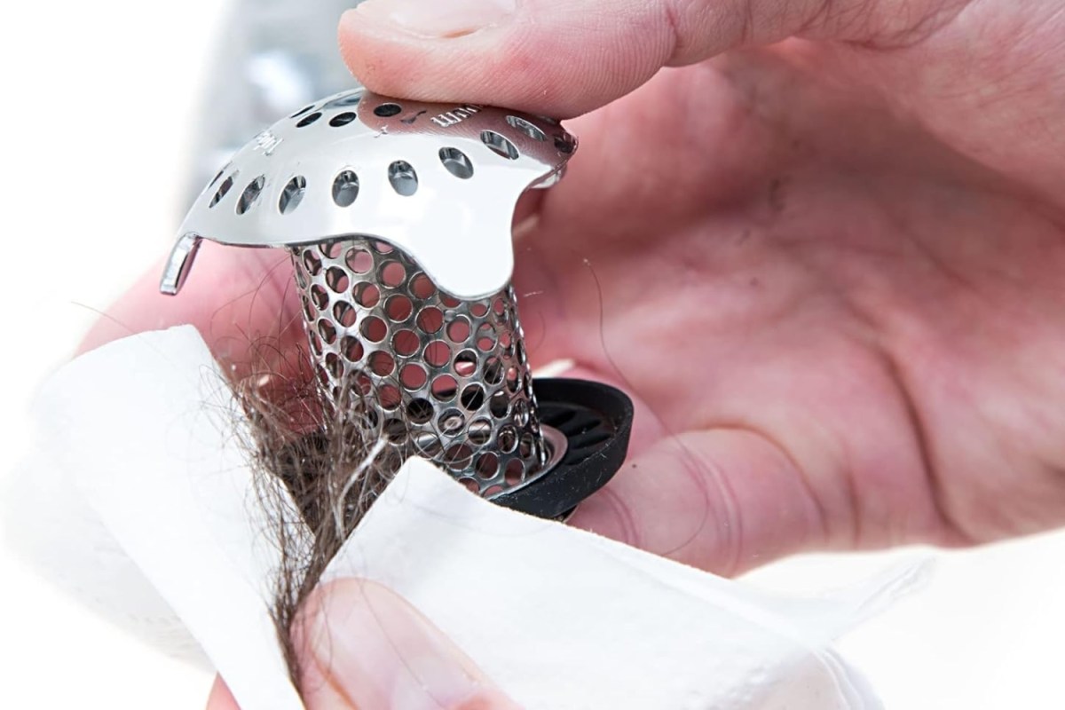 Someone removing a shower drain hair catcher full of hair