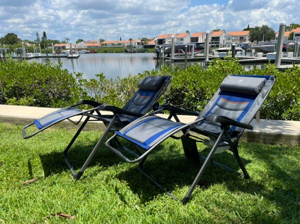 Two zero gravity chairs on grass near a river