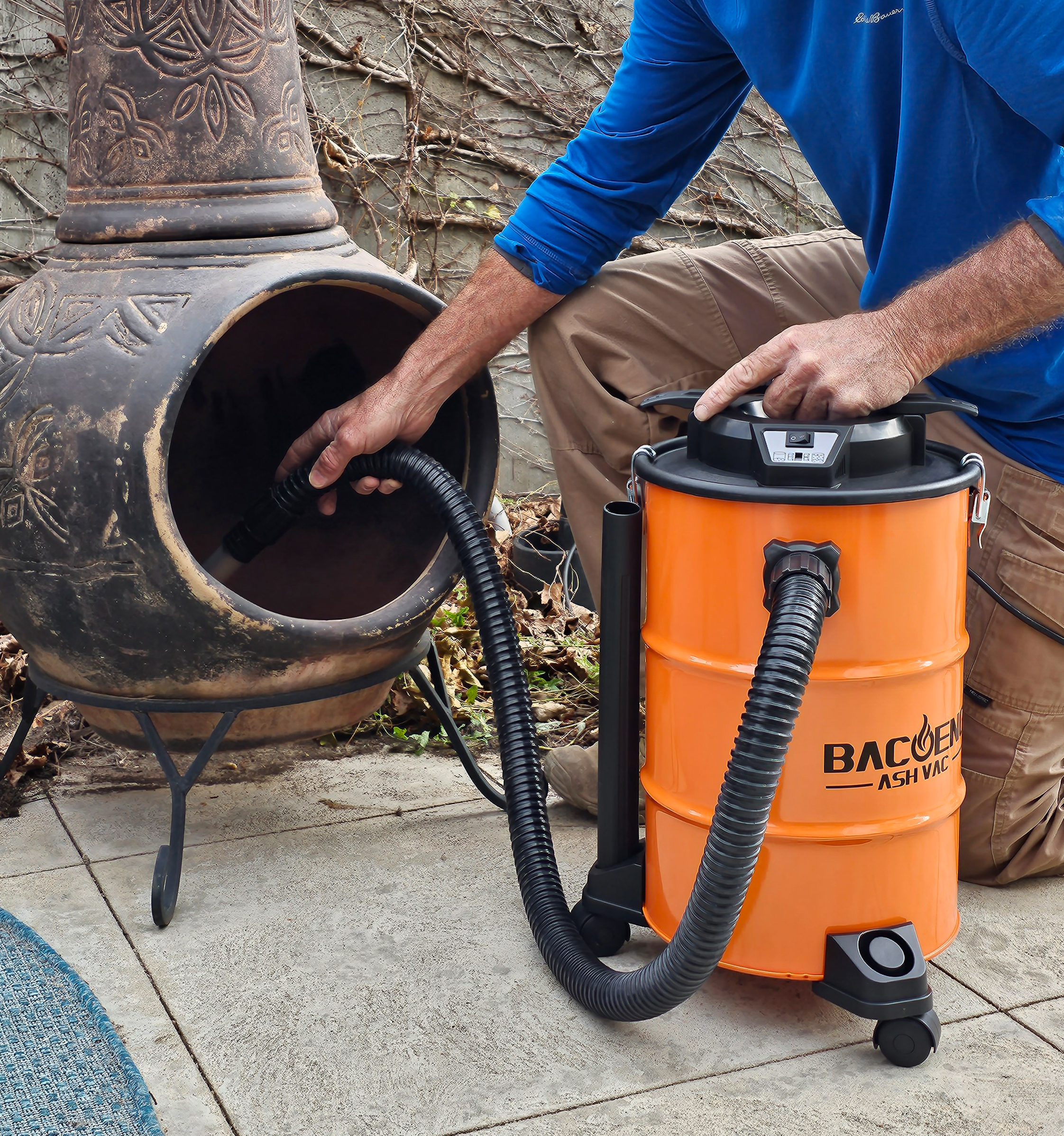 A person holding the best ash vacuum in one hand while vacuuming ash from an indoor fireplace with the other.