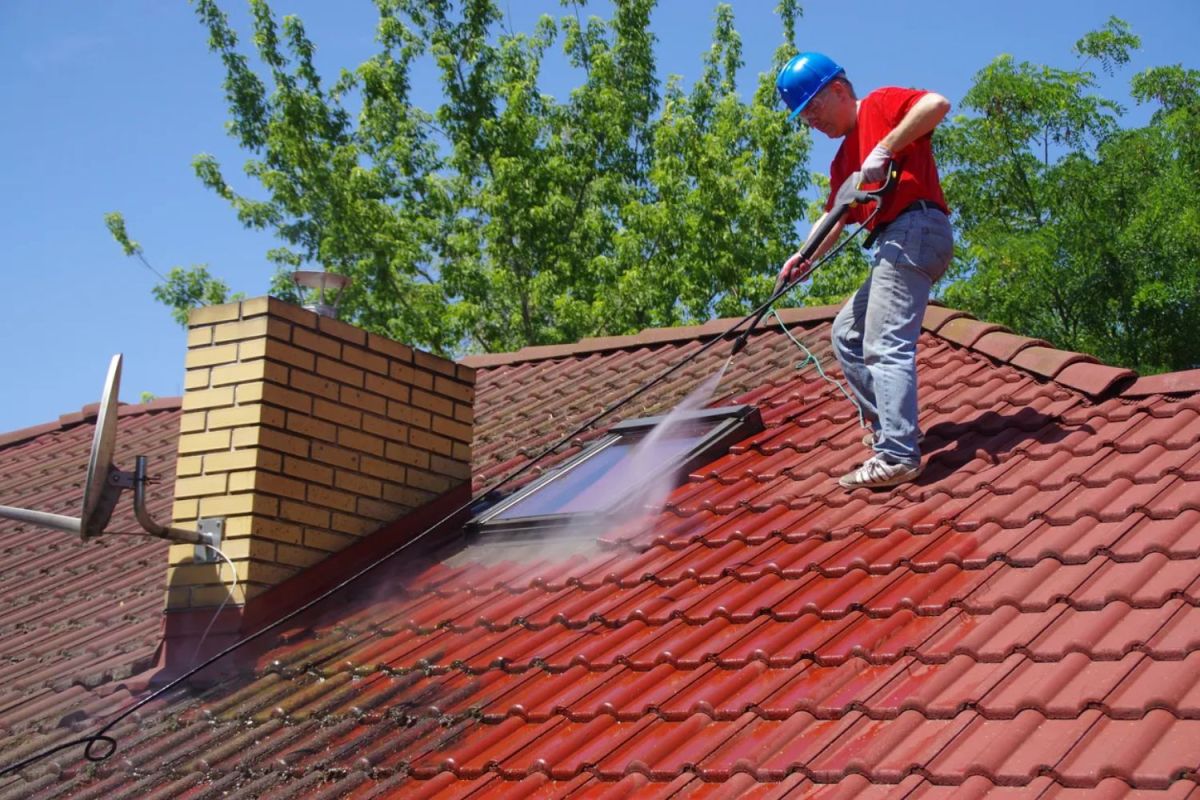 Man standing on a roof, cleaning it with a sprayer