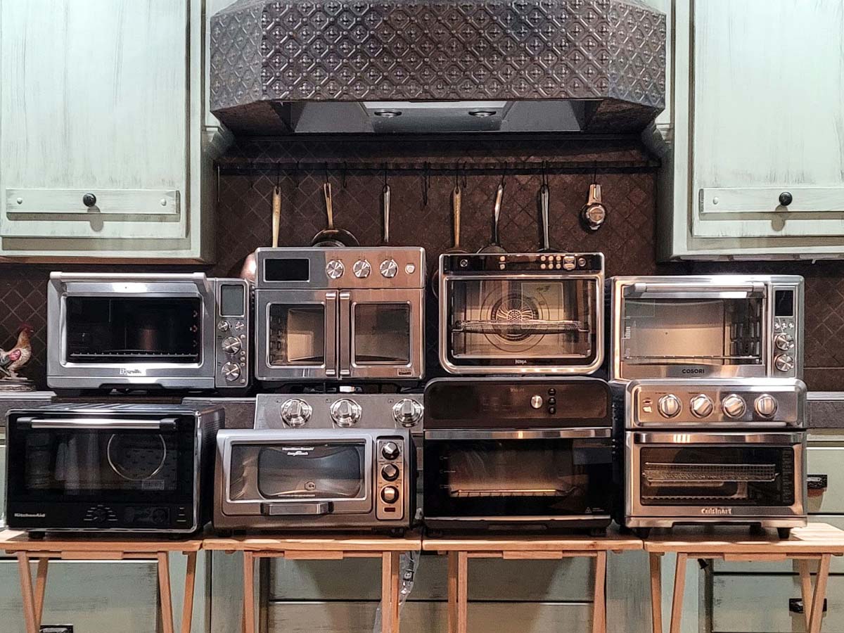 A group of the Best Air-Fryer Toaster Ovens together on a kitchen counter and row of TV trays before testing.