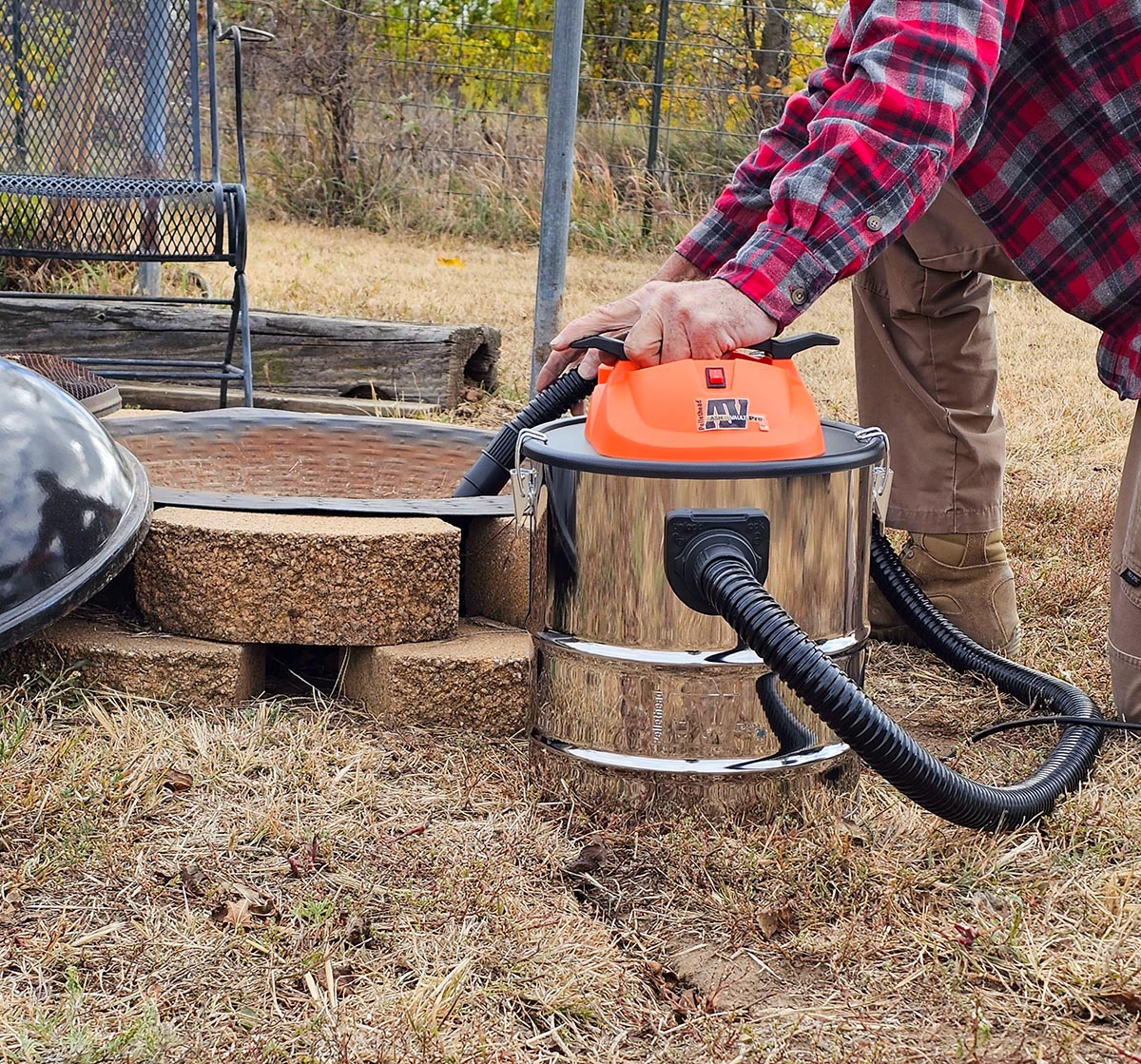 A person kneeling next to an outdoor fire pit while using the best ash vacuum option to clean it.