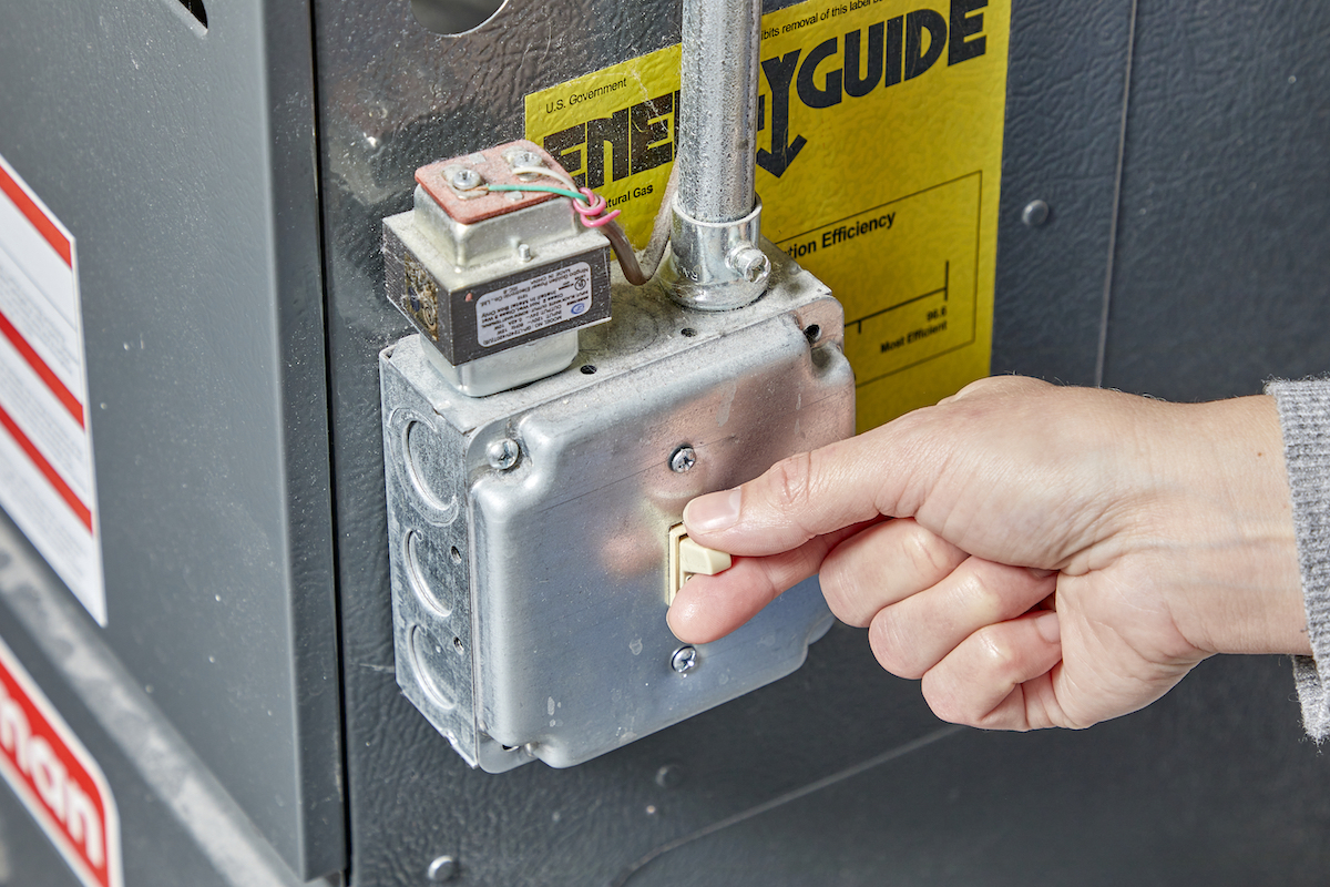 Woman toggles the switch on a furnace to the "on" position.