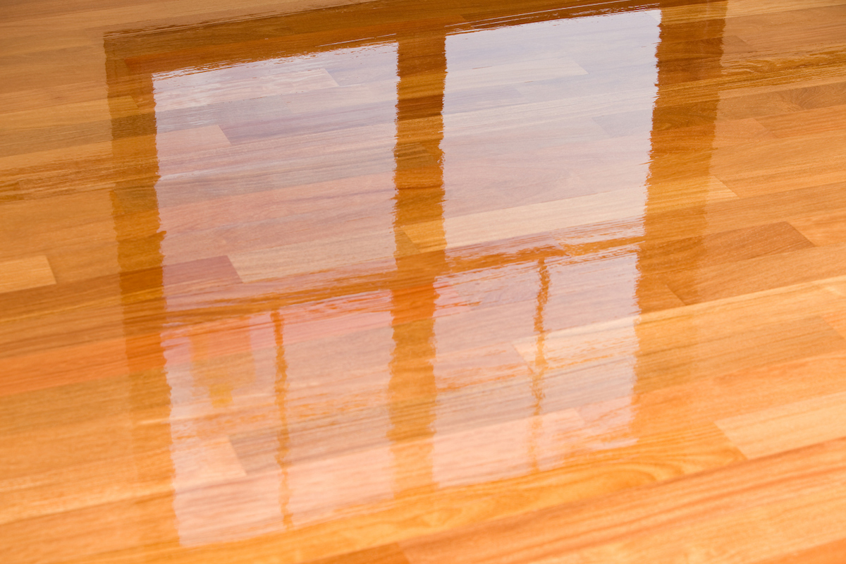 A window is reflecting on wet polyurethane on refinished hardwood flooring.