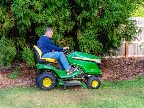 Person in blue sweatshirt and jeans driving one of the best riding mowers for hills and uneven yards