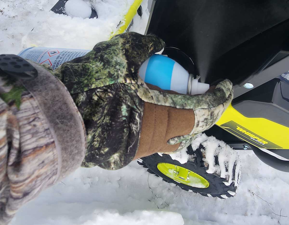 A person wearing gloves and spraying the DuPont Teflon Snow & Ice Repellent on a snow blower in the snow.