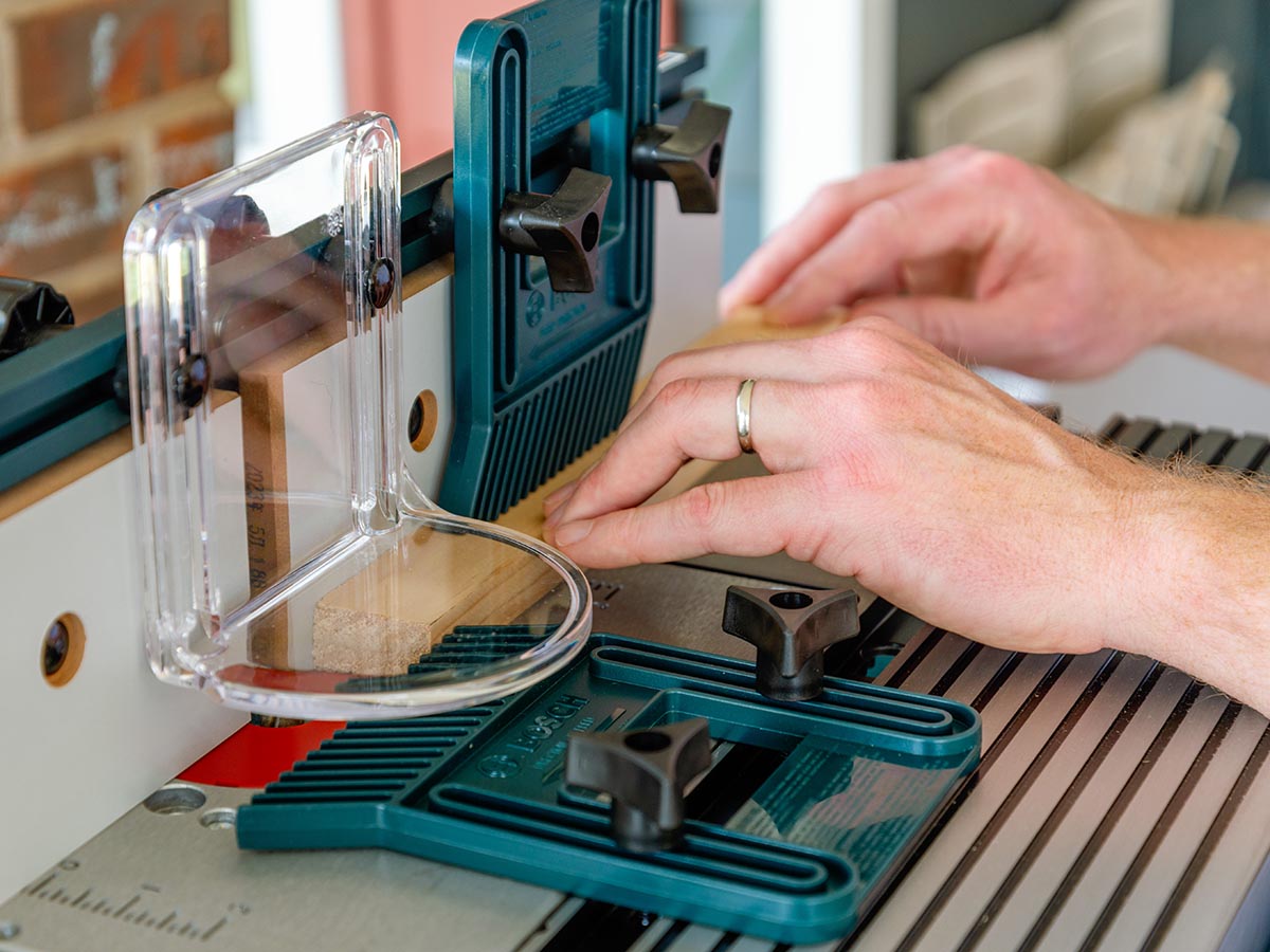 A person using a Bosch router table on a piece of wood trim during testing.