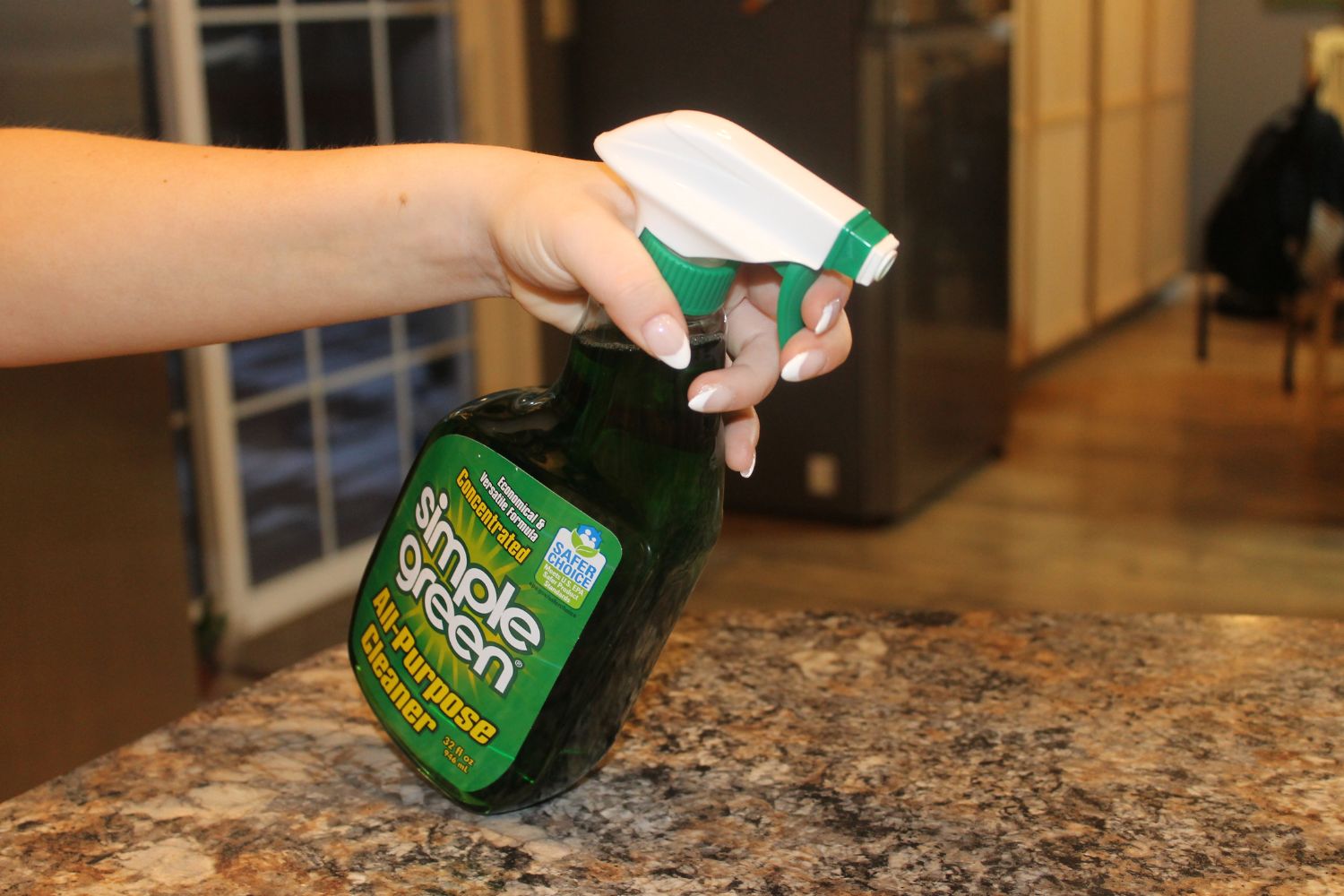 Person with French manicure spraying Simple Green clenaer on granite countertop